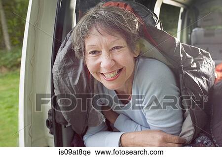 Stock Image - Portrait of senior woman inside sleeping bag, in open camper van. Fotosearch