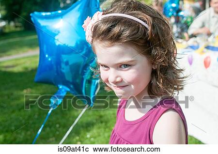 Stock Image - Portrait of young girl holding helium balloon, outdoors. Fotosearch