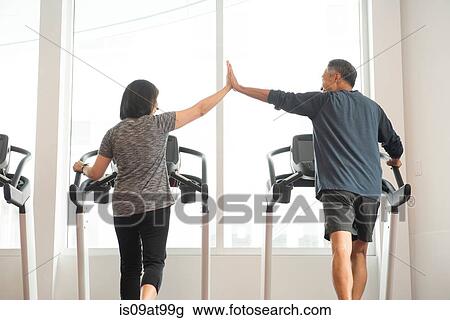 Rear view of mature couple on treadmill doing high five View Large Photo Image Stock Image - Rear view of mature couple on treadmill doing high five. Fotosearch