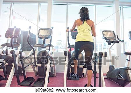 Stock Image - Rear view of mature woman at gym on step machine. Fotosearch