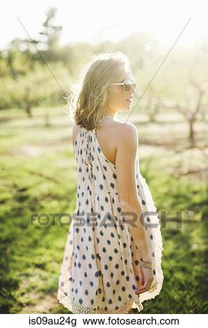 Rear view of young woman in orchard wearing sleeveless dress and sunglasses looking away View Large Photo Image Stock Image - Rear view of young woman in orchard wearing sleeveless dress and sunglasses looking away. Fotosearch