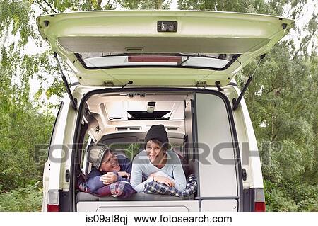 Stock Image - Senior couple lying inside open camper van. Fotosearch