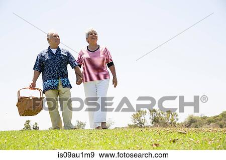 Senior couple walking hand in hand carrying picnic basket View Large Photo Image Stock Photo - Senior couple walking hand in hand carrying picnic basket. Fotosearch