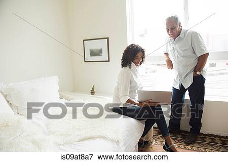 Stock Photo - Senior man and wife looking at laptop in bedroom. Fotosearch