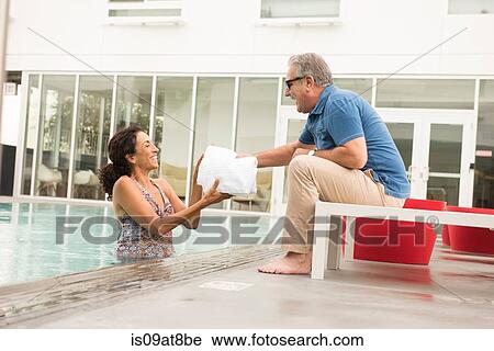 Stock Image - Senior man handing towel to wife from poolside. Fotosearch