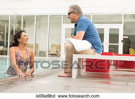 Stock Image - Senior man talking to wife from poolside. Fotosearch