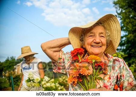 Senior woman holding onto straw hat and flowers on farm View Large Photo Image Stock Photo - Senior woman holding onto straw hat and flowers on farm. Fotosearch