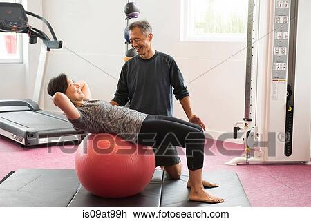 Stock Image - Side view of mature couple using excersice ball. Fotosearch