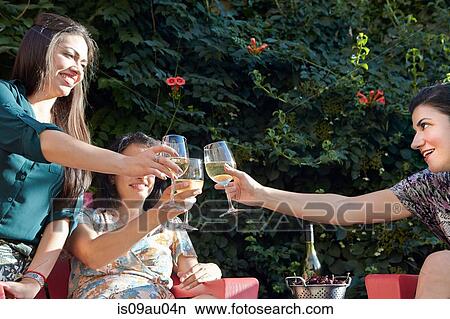Picture - Three women toating with white wine on patio. Fotosearch