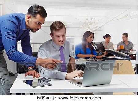 Stock Photography - Two businessmen having discussion, looking at laptop, colleagues working in background. Fotosearch