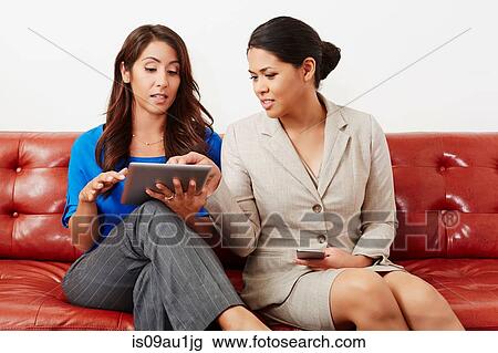 Stock Image - Two businesswomen having meeting, looking at digital tablet. Fotosearch