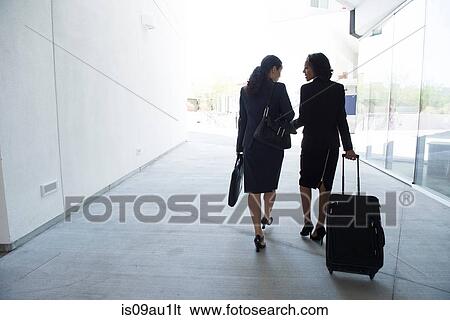 Two businesswomen in walkway, pulling suitcase, rear view View Large Photo Image Stock Photograph - Two businesswomen in walkway, pulling suitcase, rear view. Fotosearch