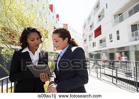 Stock Image - Two businesswomen looking at digital tablet, ouytdoors. Fotosearch
