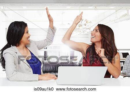 Two businesswomen sitting at desk, giving high five View Large Photo Image Stock Image - Two businesswomen sitting at desk, giving high five. Fotosearch