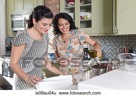 Two female friends pouring white wine in kitchen View Large Photo Image Stock Photograph - Two female friends pouring white wine in kitchen. Fotosearch