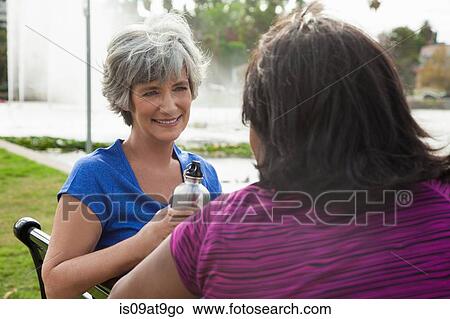 Picture - Two mature female friends sitting on park bench, rear view. Fotosearch