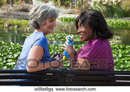 Two mature female friends sitting on park bench, laughing View Large Photo Image Stock Photography - Two mature female friends sitting on park bench, laughing. Fotosearch