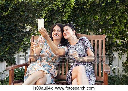 Two women taking for smartphone selfie on patio View Large Photo Image Stock Photo - Two women taking for smartphone selfie on patio. Fotosearch