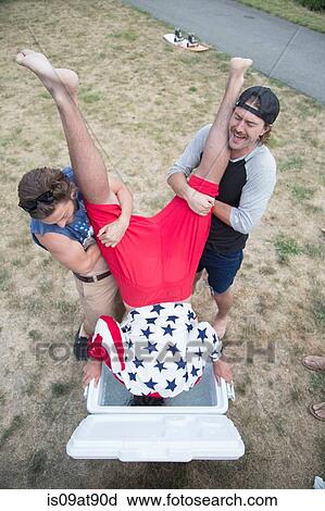 Stock Image - Two young men dunking friend into cooler on Independence Day, USA. Fotosearch