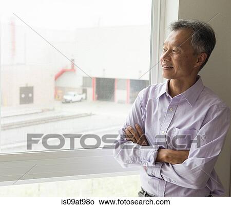 Waist up of mature man looking out of window arms crossed View Large Photo Image Picture - Waist up of mature man looking out of window arms crossed. Fotosearch