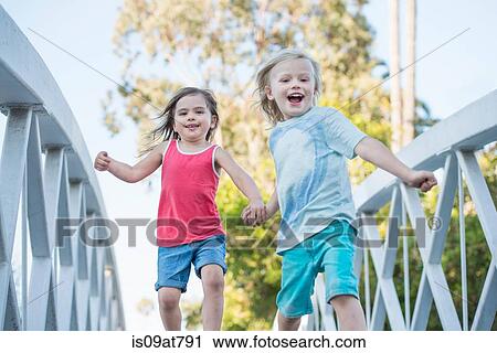 Stock Image - Young boy and girl walking over wooden footbridge, low angle view. Fotosearch