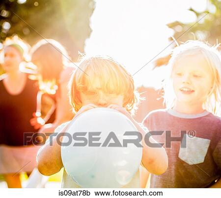Stock Image - Young boy blowing up balloon in garden. Fotosearch