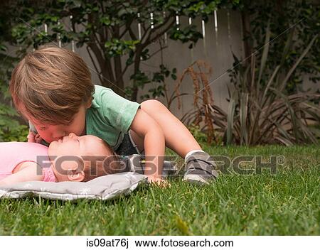 Stock Image - Young boy, kissing baby sister, outdoors. Fotosearch