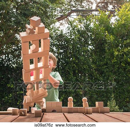Stock Photo - Young boy pushing over wooden structure made from building blocks, outdoors. Fotosearch