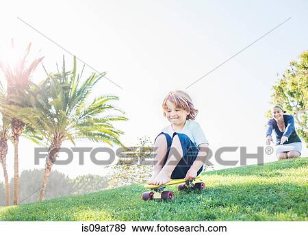 Stock Photo - Young boy sitting on skateboard, rolling down hill. Fotosearch