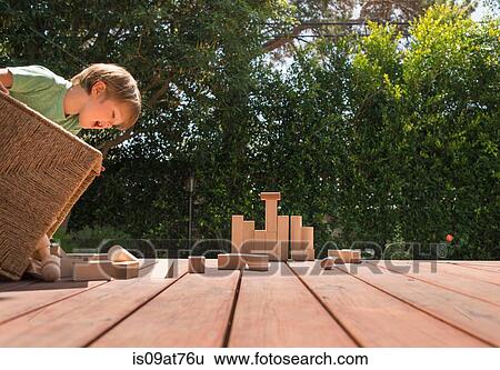 Stock Photograph - Young boy tipping wooden building blocks out on garden decking. Fotosearch