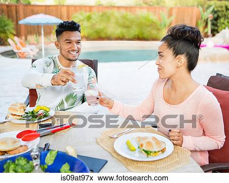 Young couple sitting down to meal outdoors making a toast View Large Photo Image Stock Photo - Young couple sitting down to meal outdoors making a toast. Fotosearch
