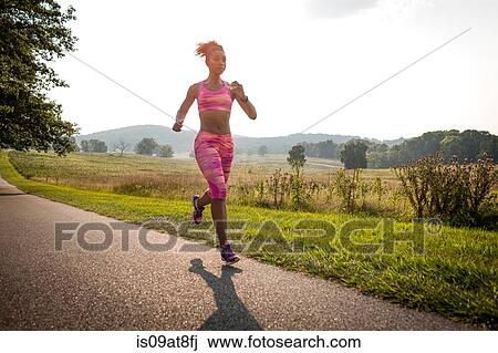 Stock Image - Young female runner running along rural park path. Fotosearch