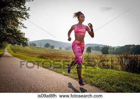 Stock Image - Young female runner running in rural park. Fotosearch