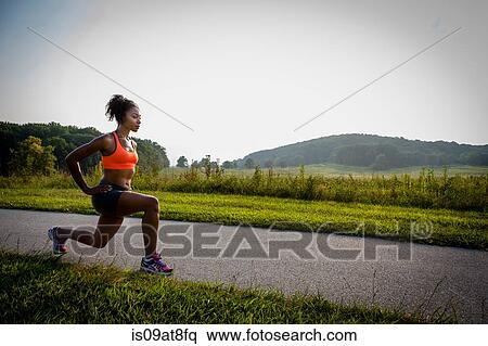 Stock Photography - Young female runner stretching on rural park path. Fotosearch