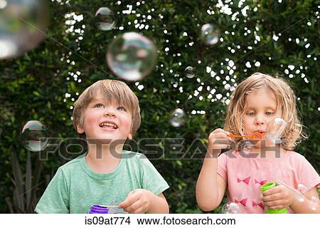 Young girl and boy blowing bubbles, outdoors View Large Photo Image Picture - Young girl and boy blowing bubbles, outdoors. Fotosearch