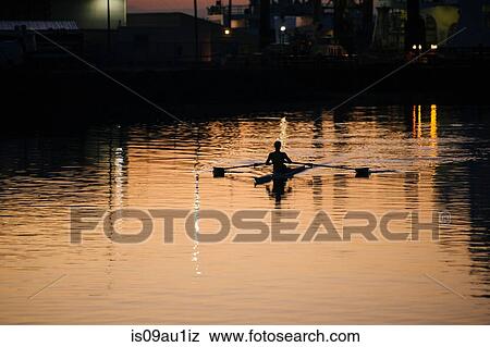 Stock Photo - Young man rowing on river at sunset. Fotosearch