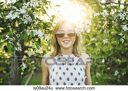 Young woman in orchard, flower in hair, wearing sunglasses looking at camera smiling View Large Photo Image Stock Photograph - Young woman in orchard, flower in hair, wearing sunglasses looking at camera smiling. Fotosearch