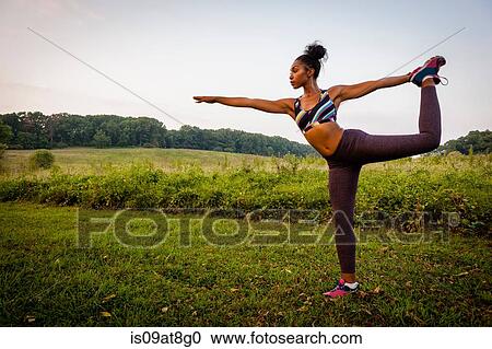 Stock Image - Young woman practicing yoga pose in rural park. Fotosearch