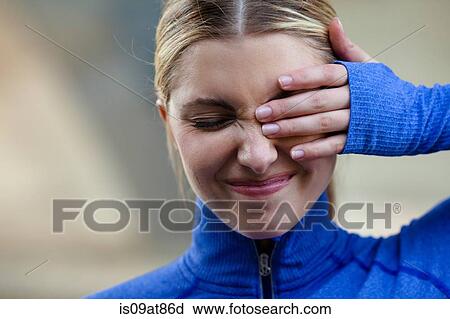 Stock Image - Young woman squinting at discomfort in eye. Fotosearch