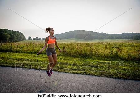 Stock Photography - Young woman training with skipping rope in rural park. Fotosearch