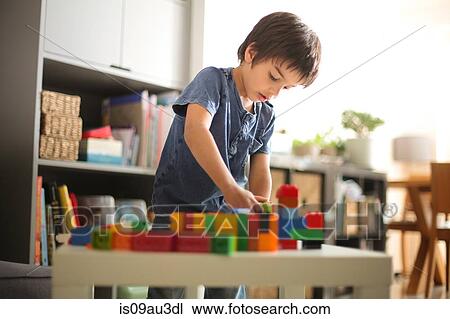 Stock Image - Boy at home looking down playing with colourful building blocks. Fotosearch