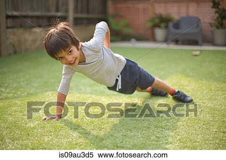 Stock Photography - Boy doing one handed push up on grass looking at camera smiling. Fotosearch