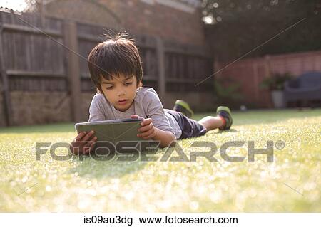Boy in garden lying on front on grass looking down using digital tablet View Large Photo Image Stock Image - Boy in garden lying on front on grass looking down using digital tablet. Fotosearch