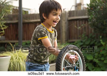Stock Image - Boy in garden repairing upside down bicycle smiling. Fotosearch