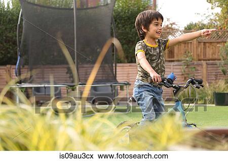 Stock Photo - Boy in garden sitting on bicycle looking away pointing. Fotosearch