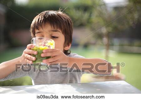 Stock Image - Boy looking down drinking green smoothie. Fotosearch