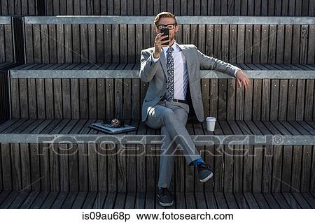 Stock Photography - Cool young businessman reading smartphone on city stair. Fotosearch