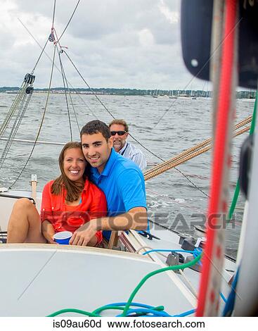 Stock Image - Couple relaxing on sailboat, looking at camera smiling. Fotosearch