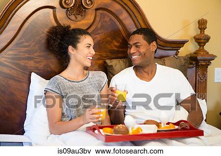 Couple sitting in bed having breakfast face to face smiling View Large Photo Image Stock Photo - Couple sitting in bed having breakfast face to face smiling. Fotosearch