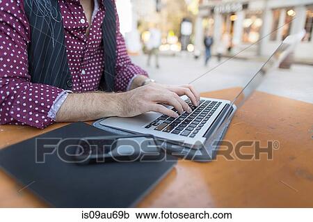 Stock Image - Cropped view of young businessman typing on laptop at sidewalk cafe. Fotosearch